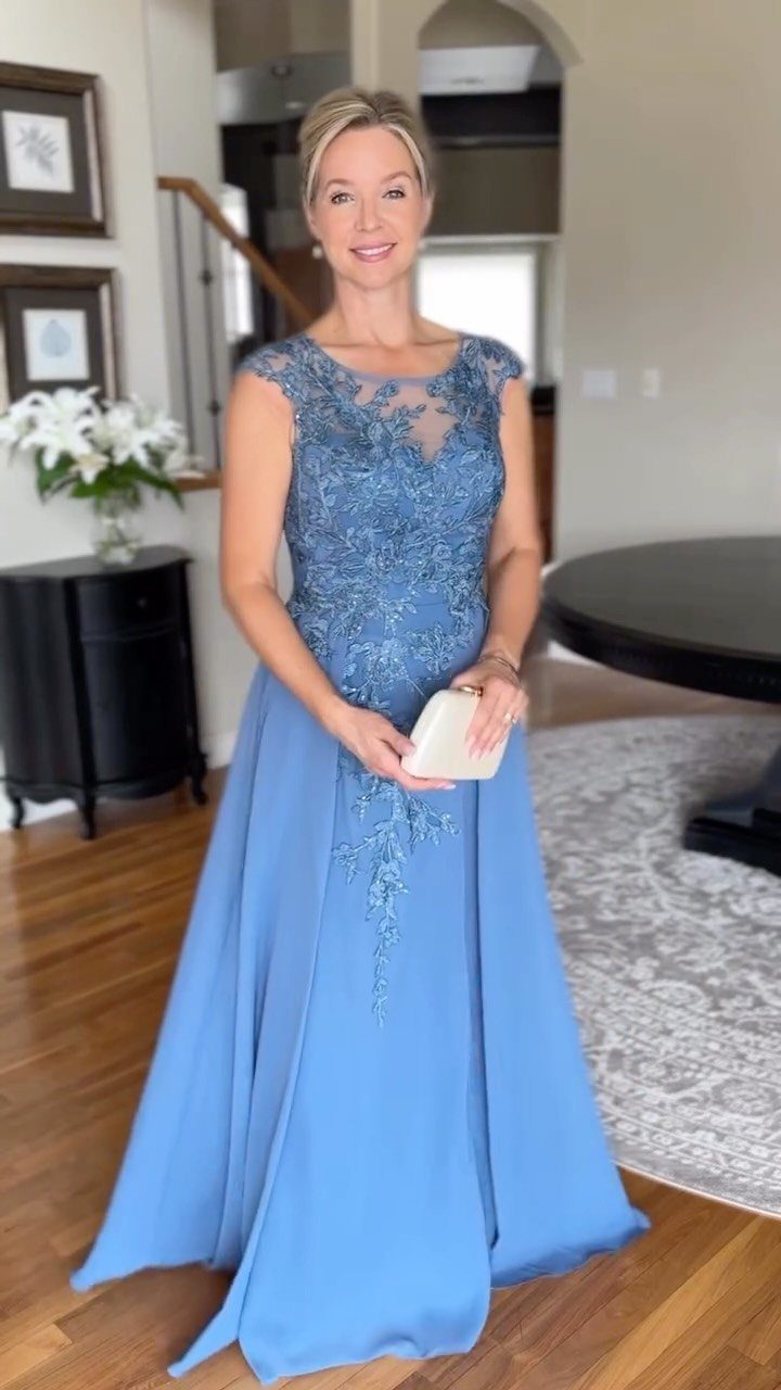 Woman in a light blue lace evening gown holding a white clutch bag.