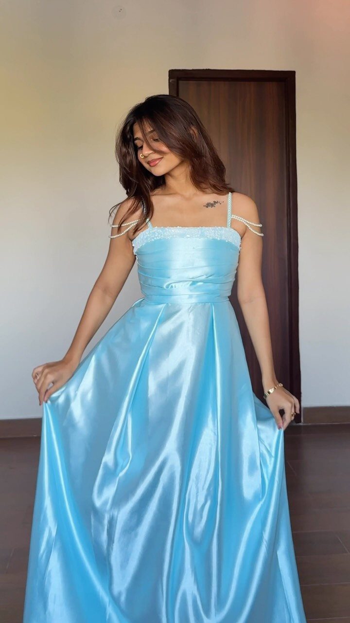 Woman in a light blue satin fit and flare gown standing indoors.
