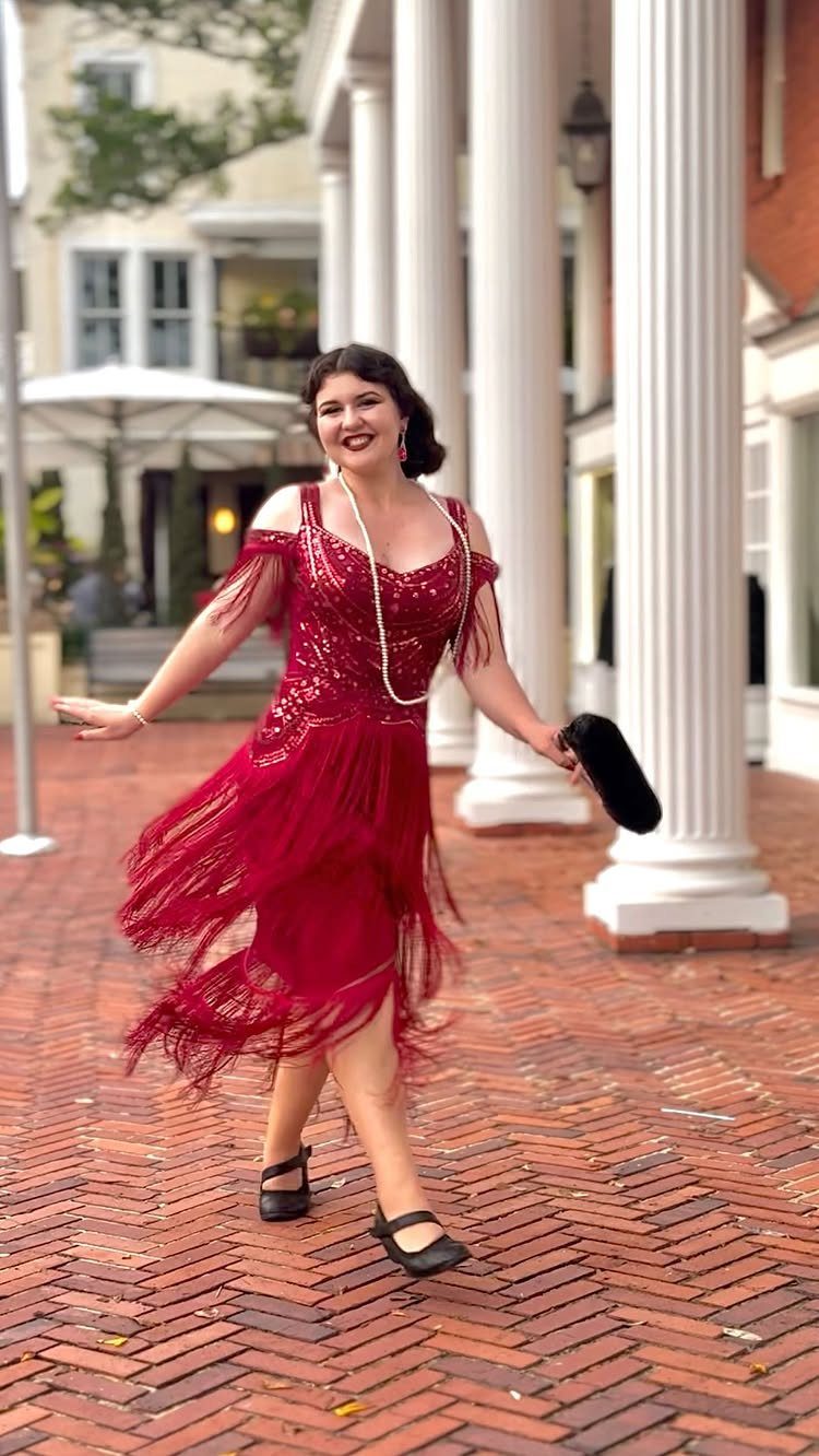 Woman in a red sequined fringe dress posing on a brick walkway with columns.