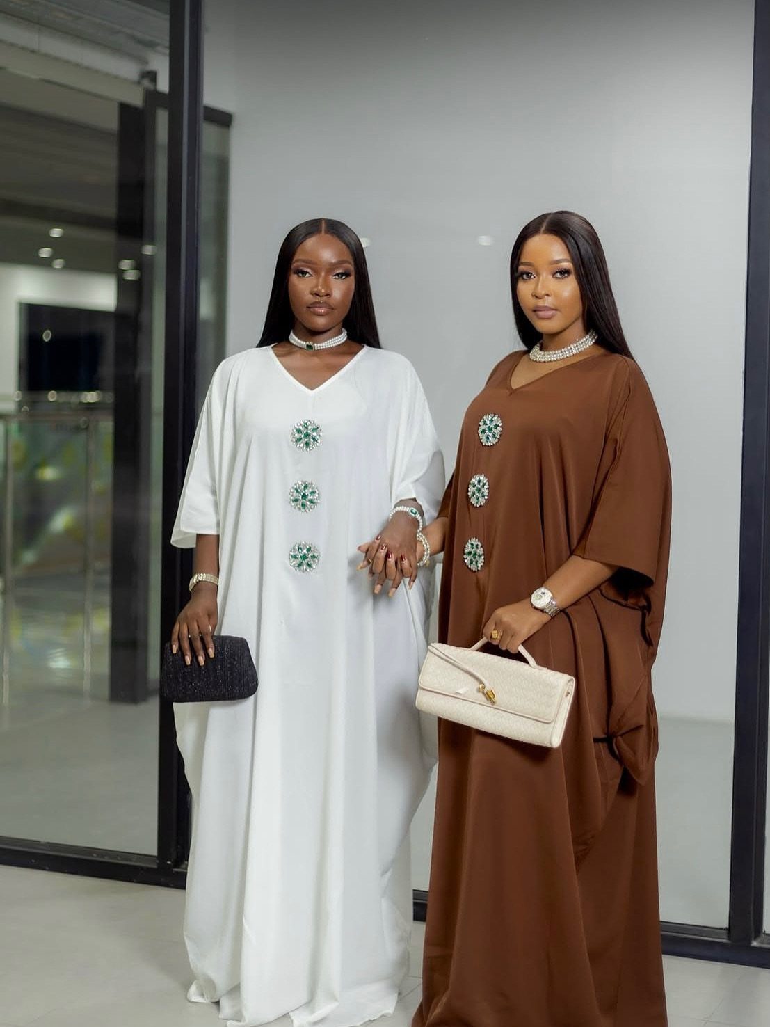Two women wearing loose-fitting white and brown kaftan dresses with circular embellishments.