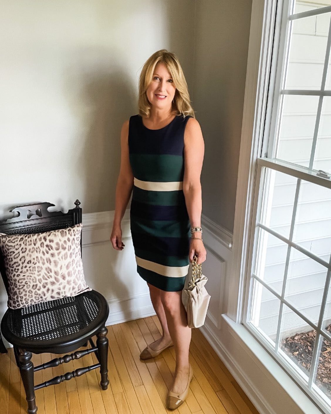 Woman wearing a striped navy and green sheath dress with tan pumps indoors.