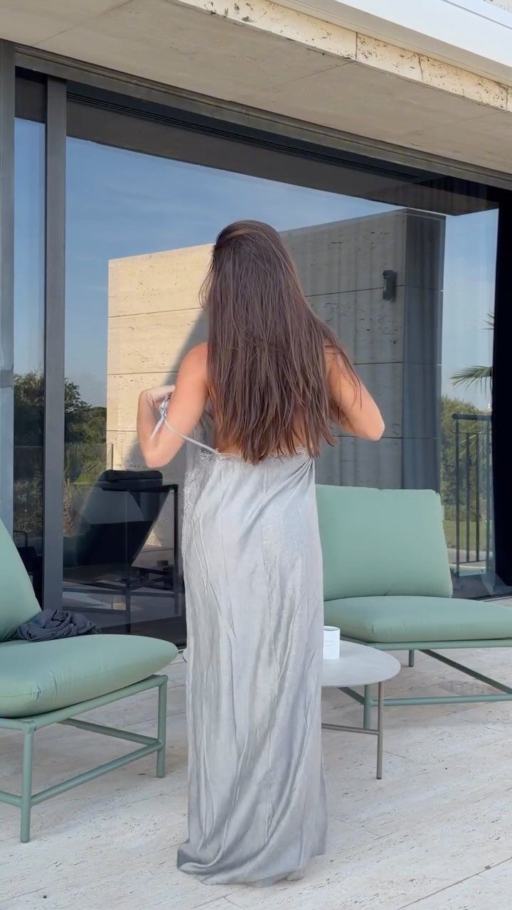 Woman from behind wearing a long silver satin slip dress on a modern patio.