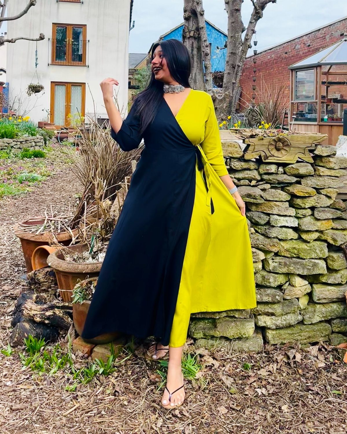 Woman in a black and yellow two-toned wrap dress standing in a garden.