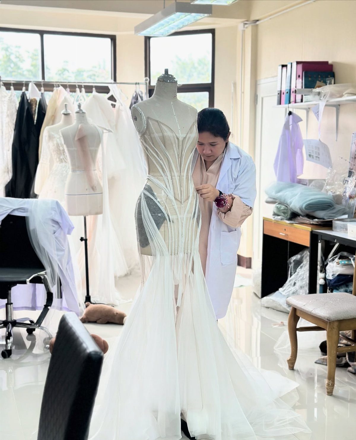 Woman tailoring a white wedding dress on a mannequin in a bright bridal studio