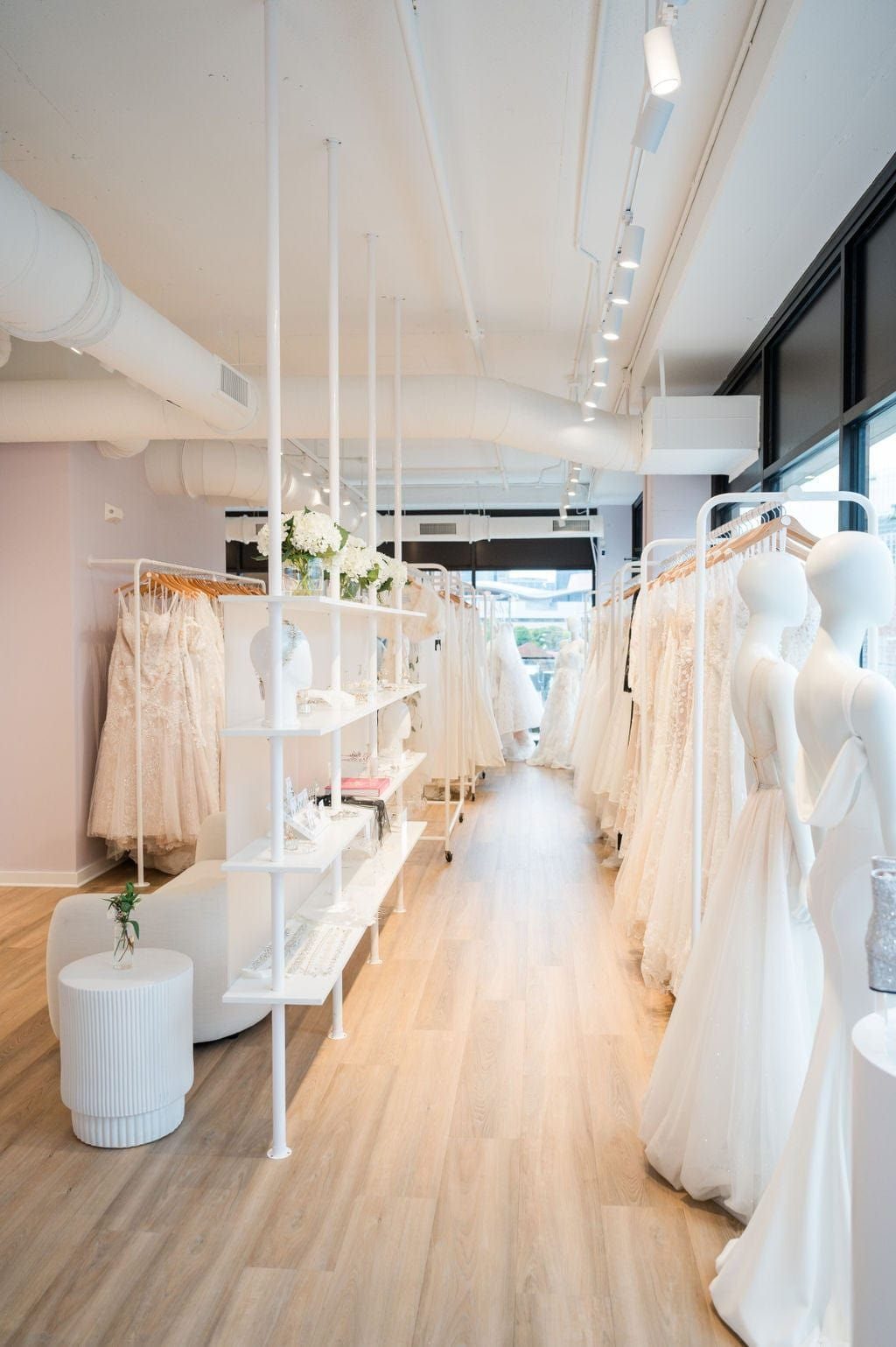 Rows of white wedding dresses on racks and mannequins in a bright bridal boutique.