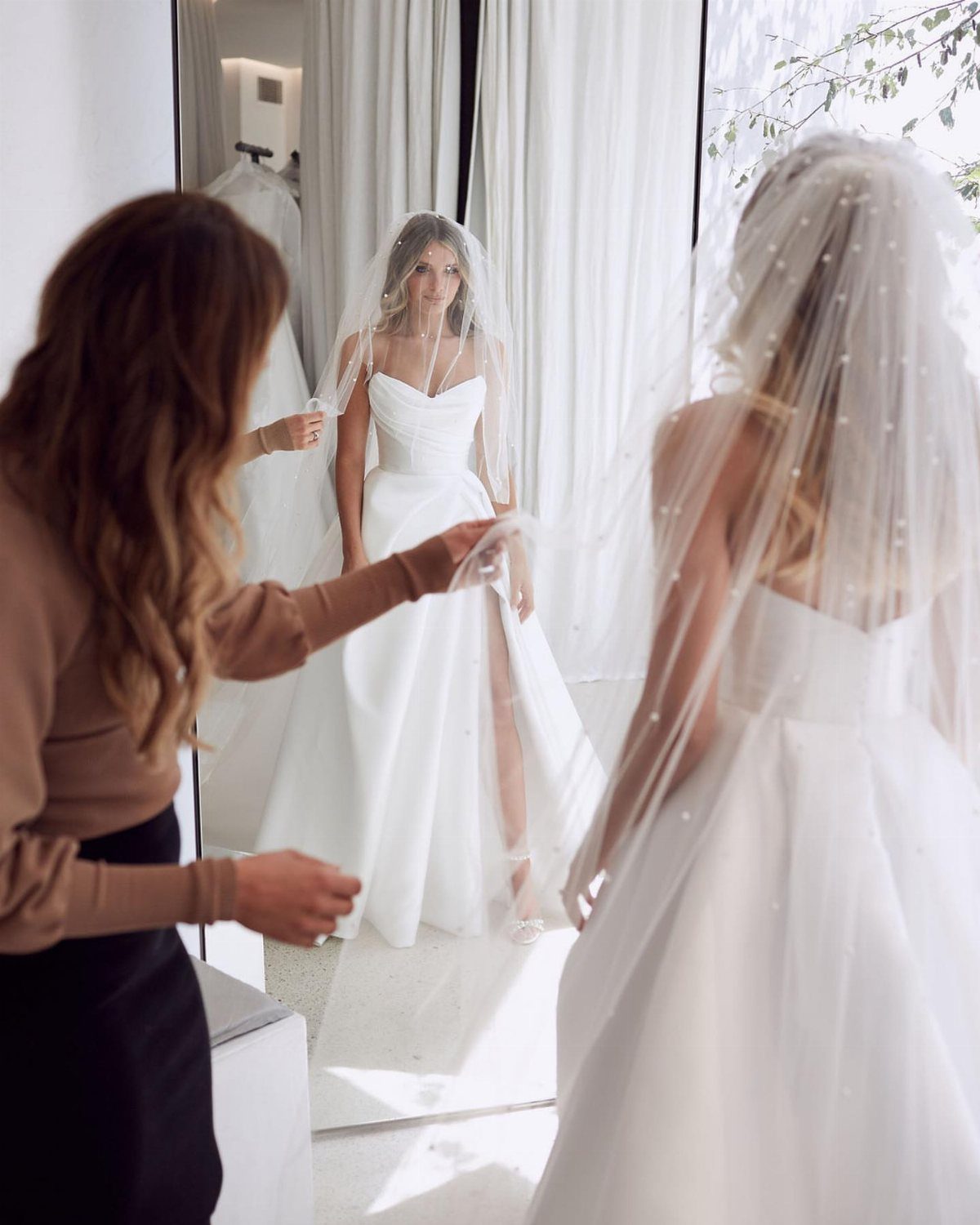 Woman in a white strapless wedding gown being fitted by a stylist in a mirror