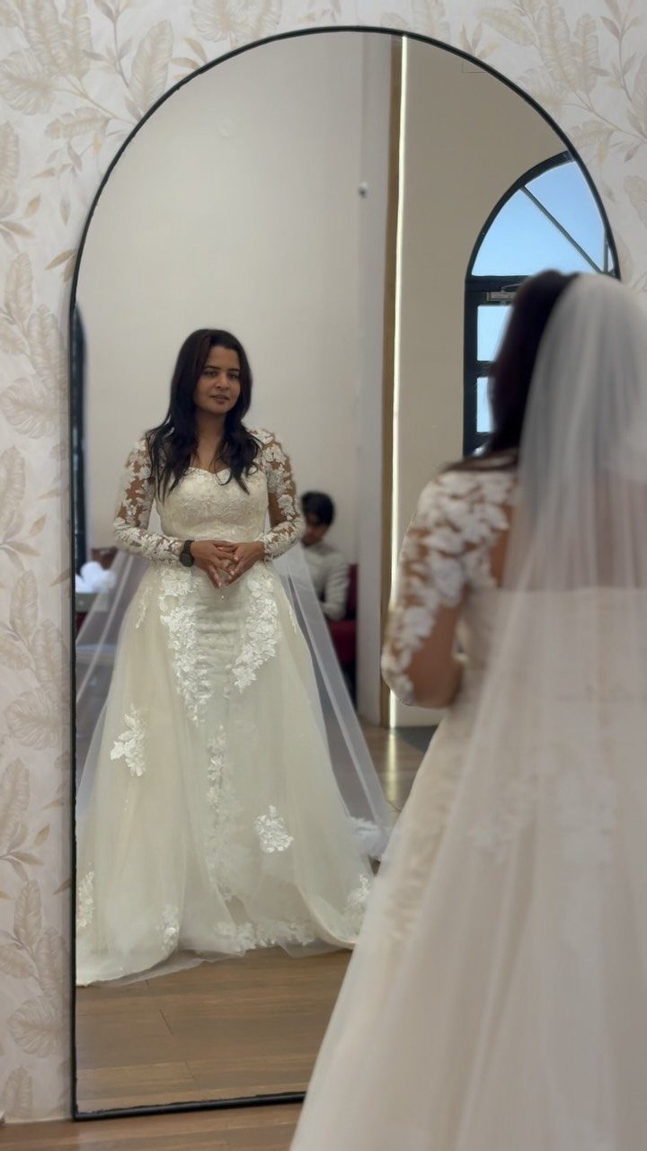 Woman in a white lace wedding gown with long sleeves reflected in a mirror.