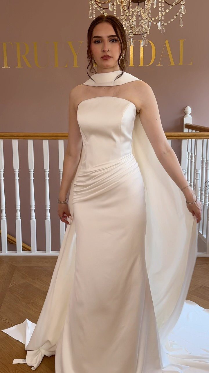 Woman in a cream satin wedding gown with a draped waist and capelet.