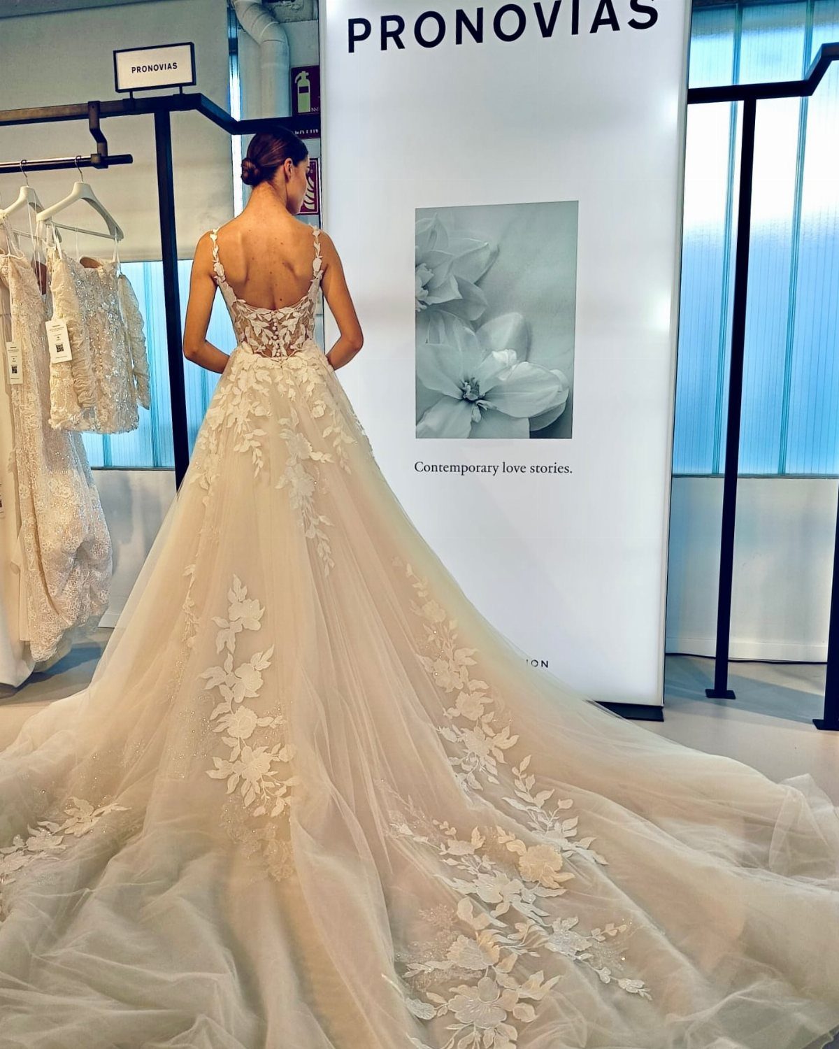 Woman in a white lace wedding gown standing before a Pronovias brand sign.