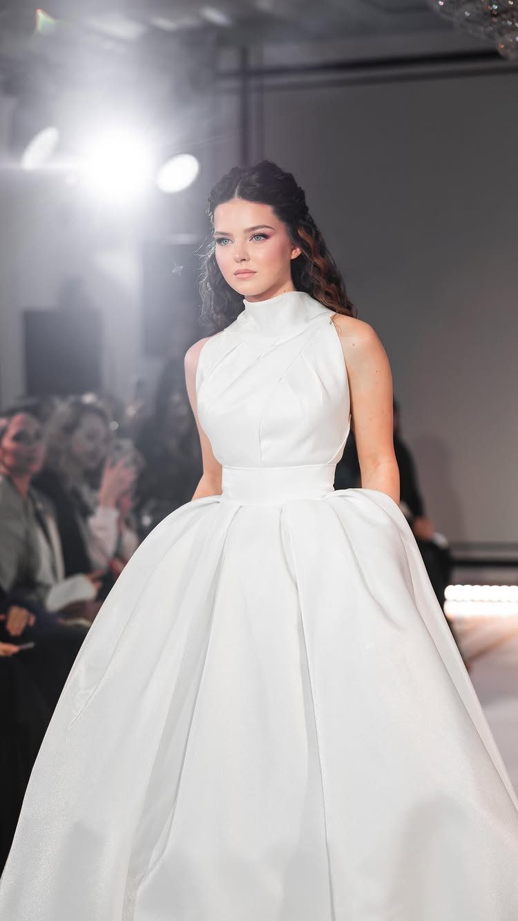 Woman wearing a white high-neck wedding gown with a voluminous ballgown skirt on runway.