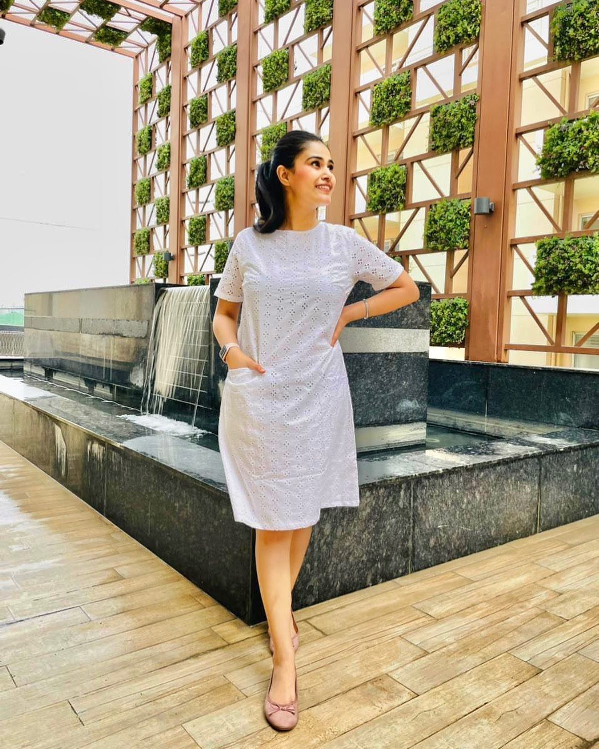 Woman in a short-sleeved white cotton dress posing by a modern outdoor water feature.