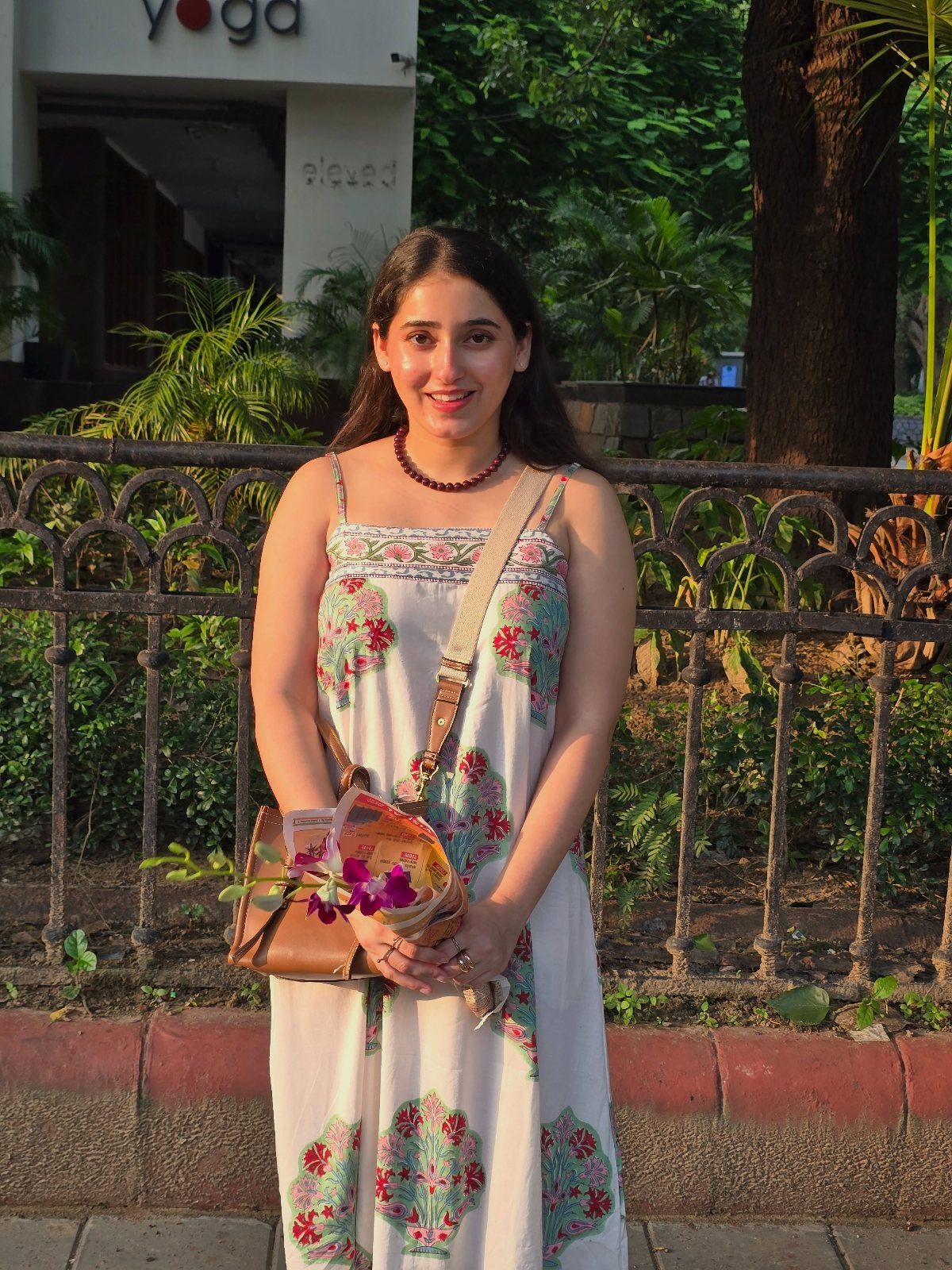Woman wearing a white cotton dress with floral embroidery and a brown shoulder bag.