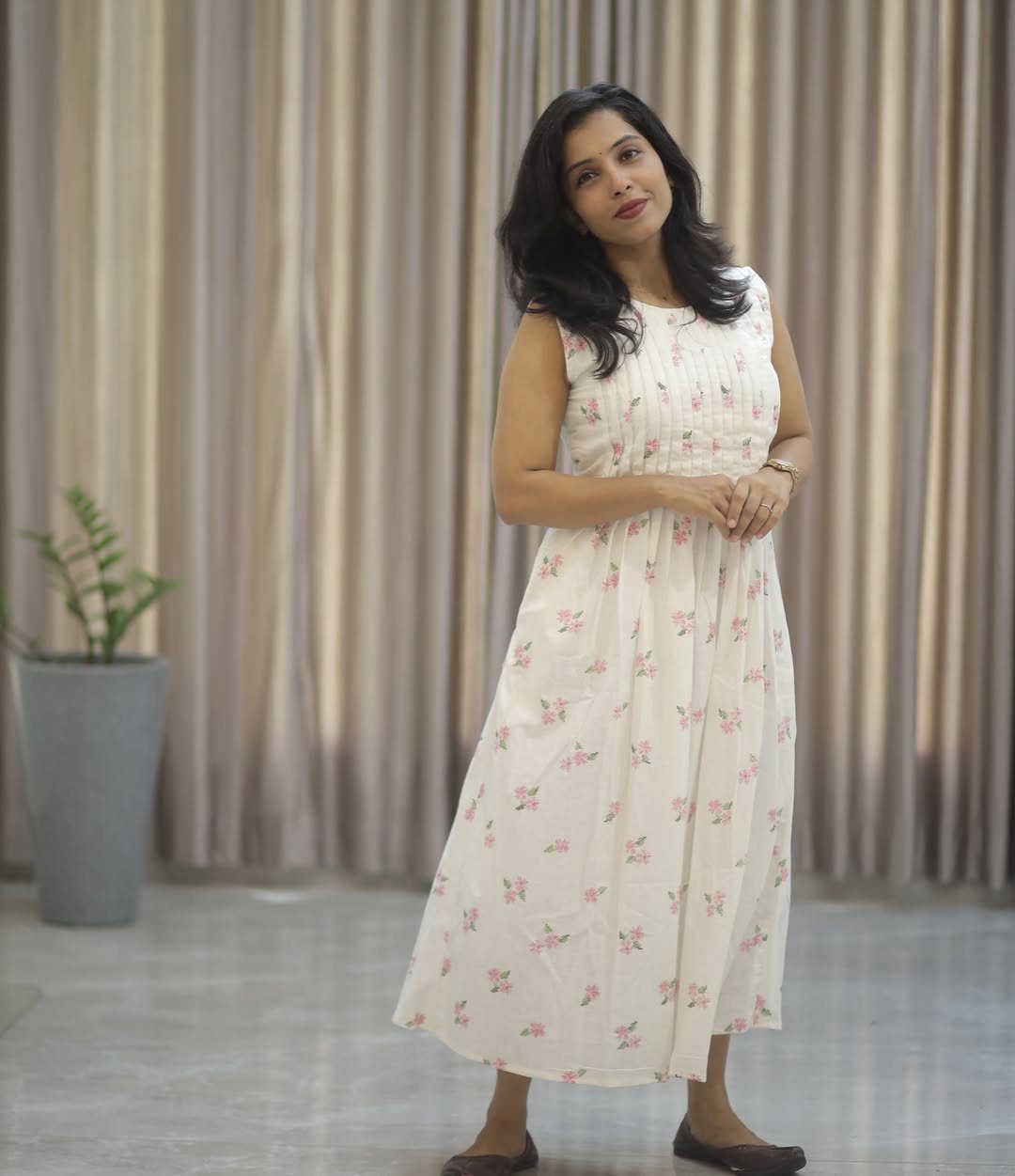 Woman wearing a sleeveless white cotton midi dress with pink floral patterns.