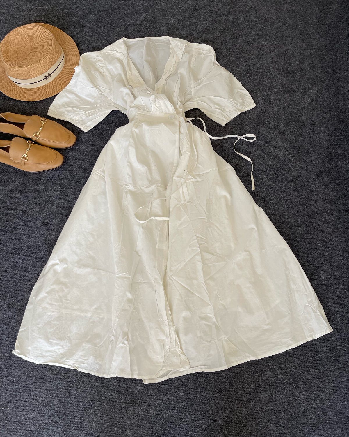 White cotton maxi dress laid flat with a straw hat and tan loafers.