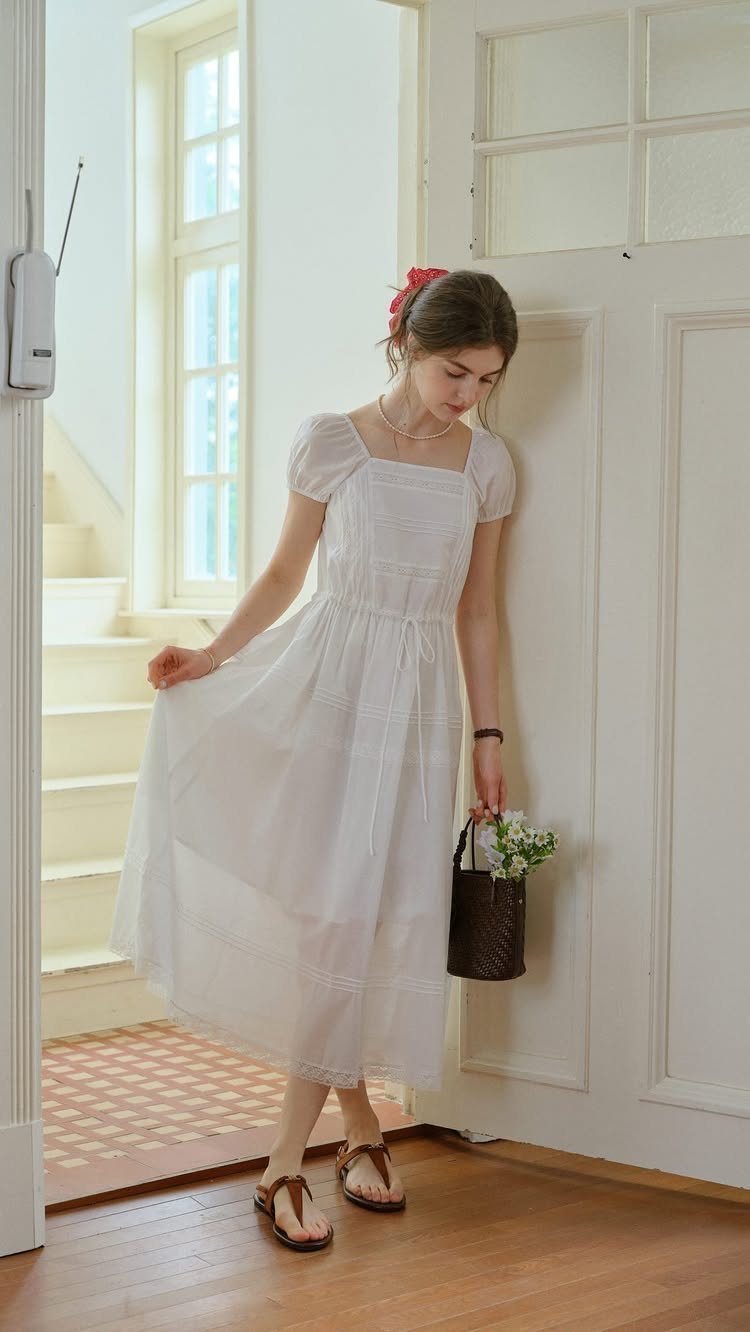 Woman in a white cotton midi dress holding a small brown woven basket.
