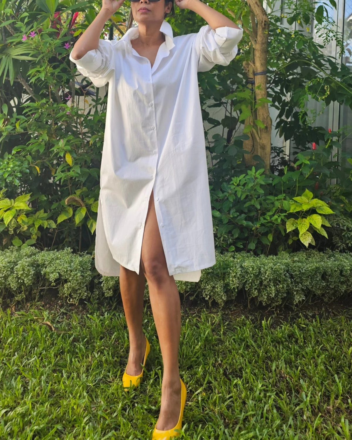 Woman in a white cotton shirt dress and yellow heels standing on green grass.