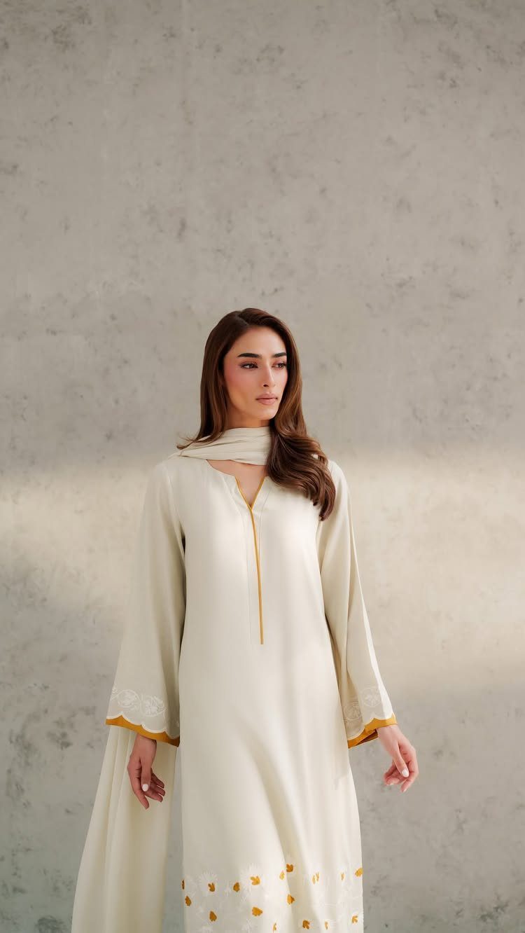 Woman in a cream-colored long dress with gold embroidery and matching scarf.