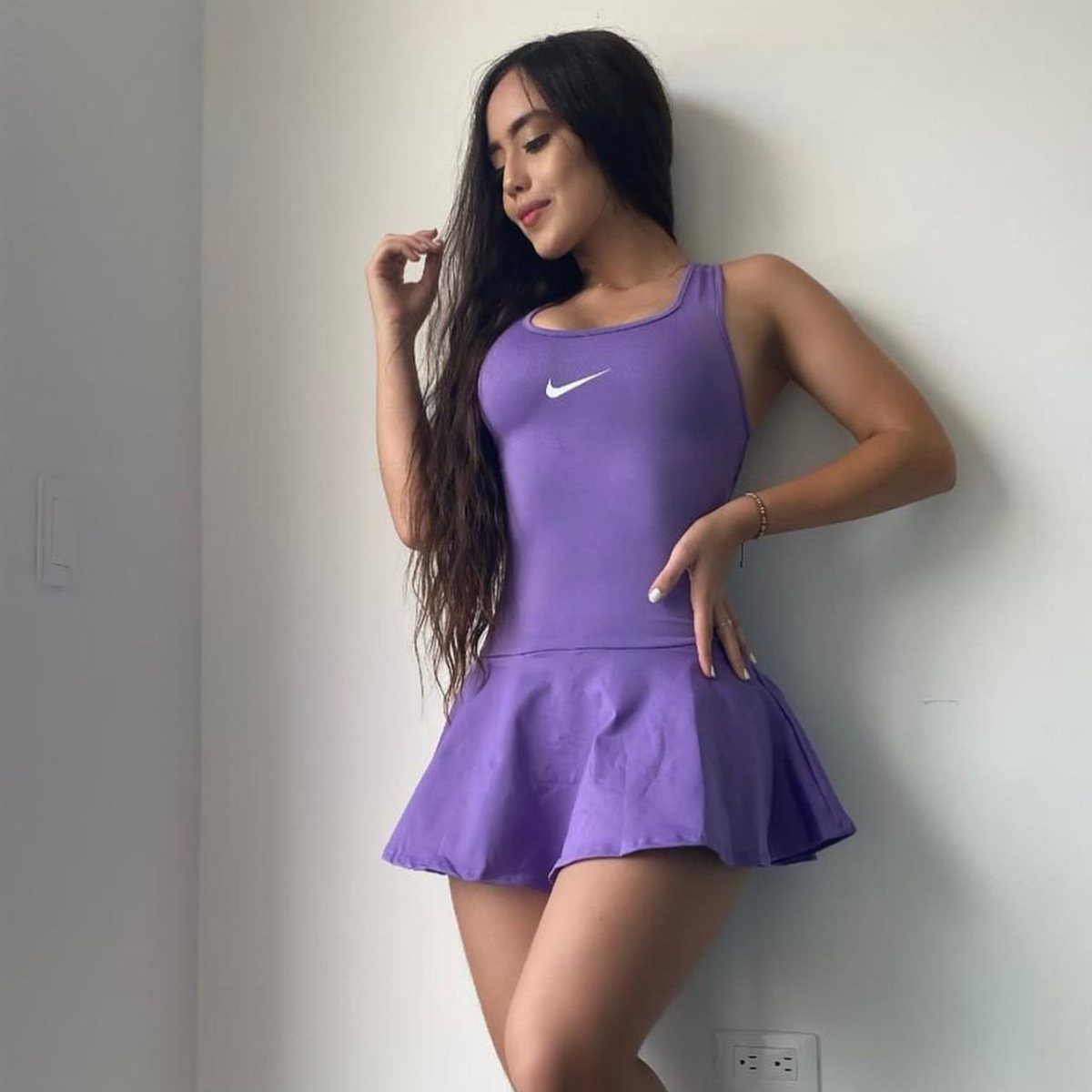 Woman wearing a purple sleeveless athletic dress with a flared skirt against white wall