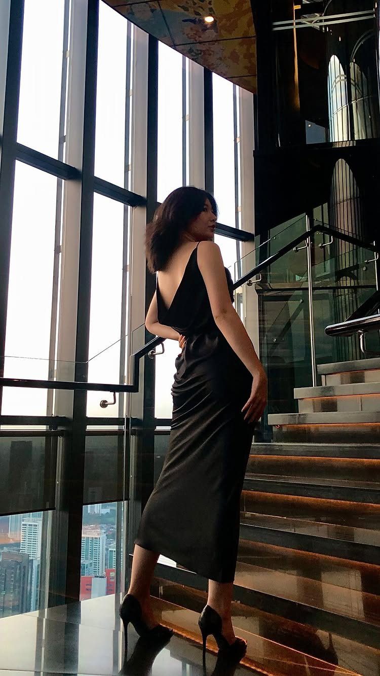 Woman in a black satin midi slip dress and heels on a staircase.