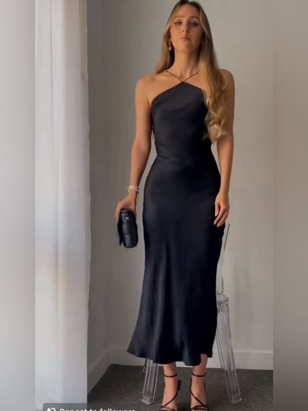 10 Zara Party Dresses to Wear This Season 2 Woman wearing a black satin one-shoulder midi dress with a black clutch bag.