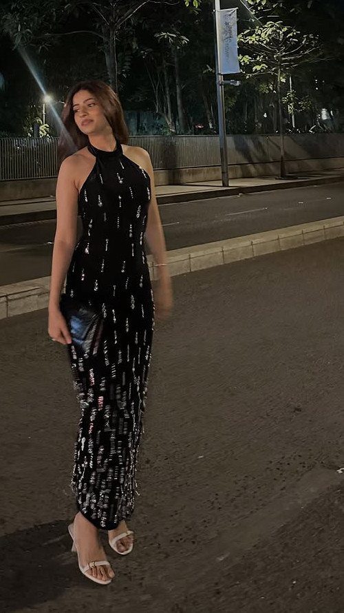 10 Zara Party Dresses to Wear This Season 9 Woman in a black sequined halter-neck maxi dress standing on a city street.