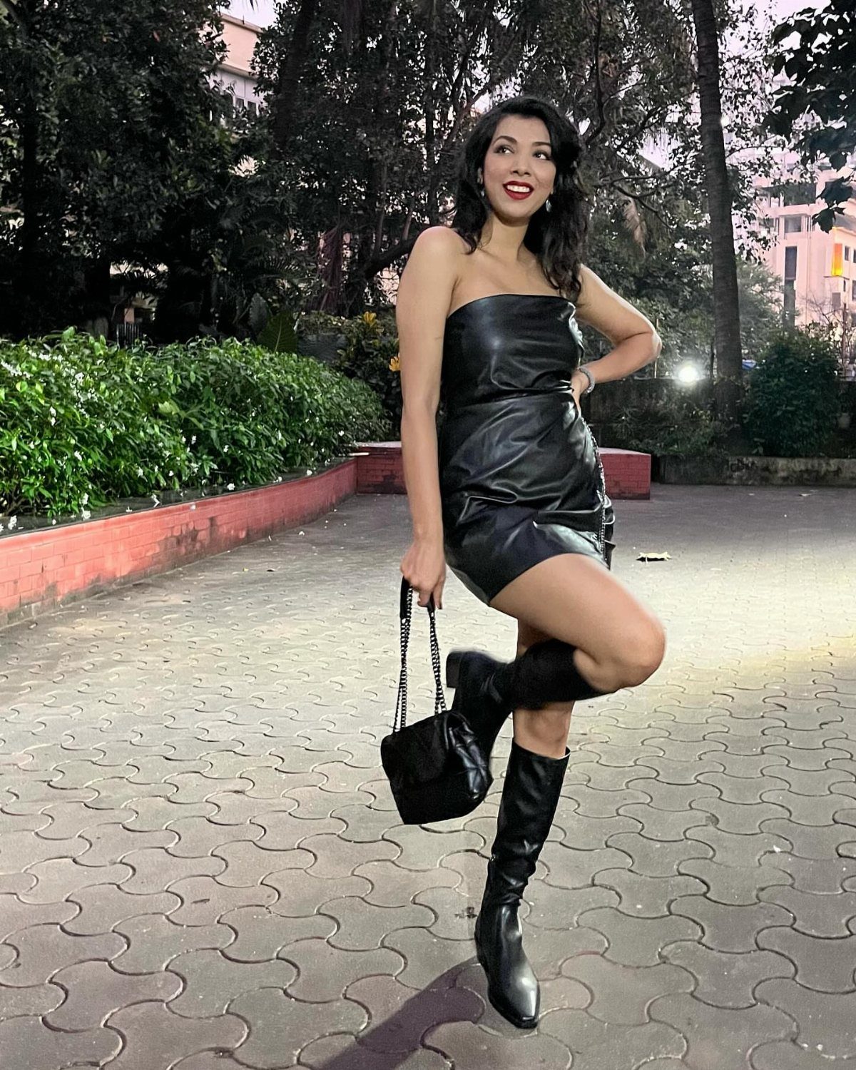 10 Zara Party Dresses to Wear This Season 6 Woman in a black strapless leather mini dress and knee-high boots posing outdoors.