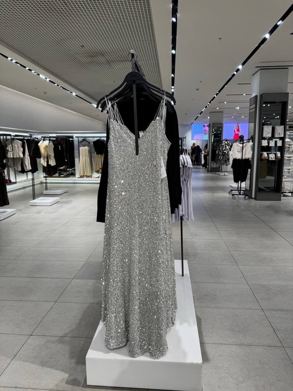 10 Zara Party Dresses to Wear This Season 3 Silver sequined midi slip dress with thin straps hanging in a retail store.
