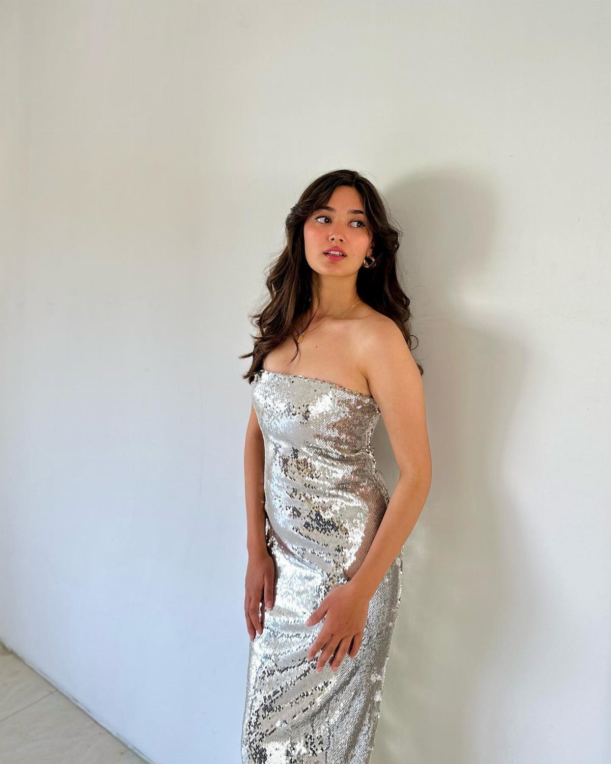 10 Zara Party Dresses to Wear This Season 10 Woman wearing a strapless silver sequined midi dress posing against a white wall.